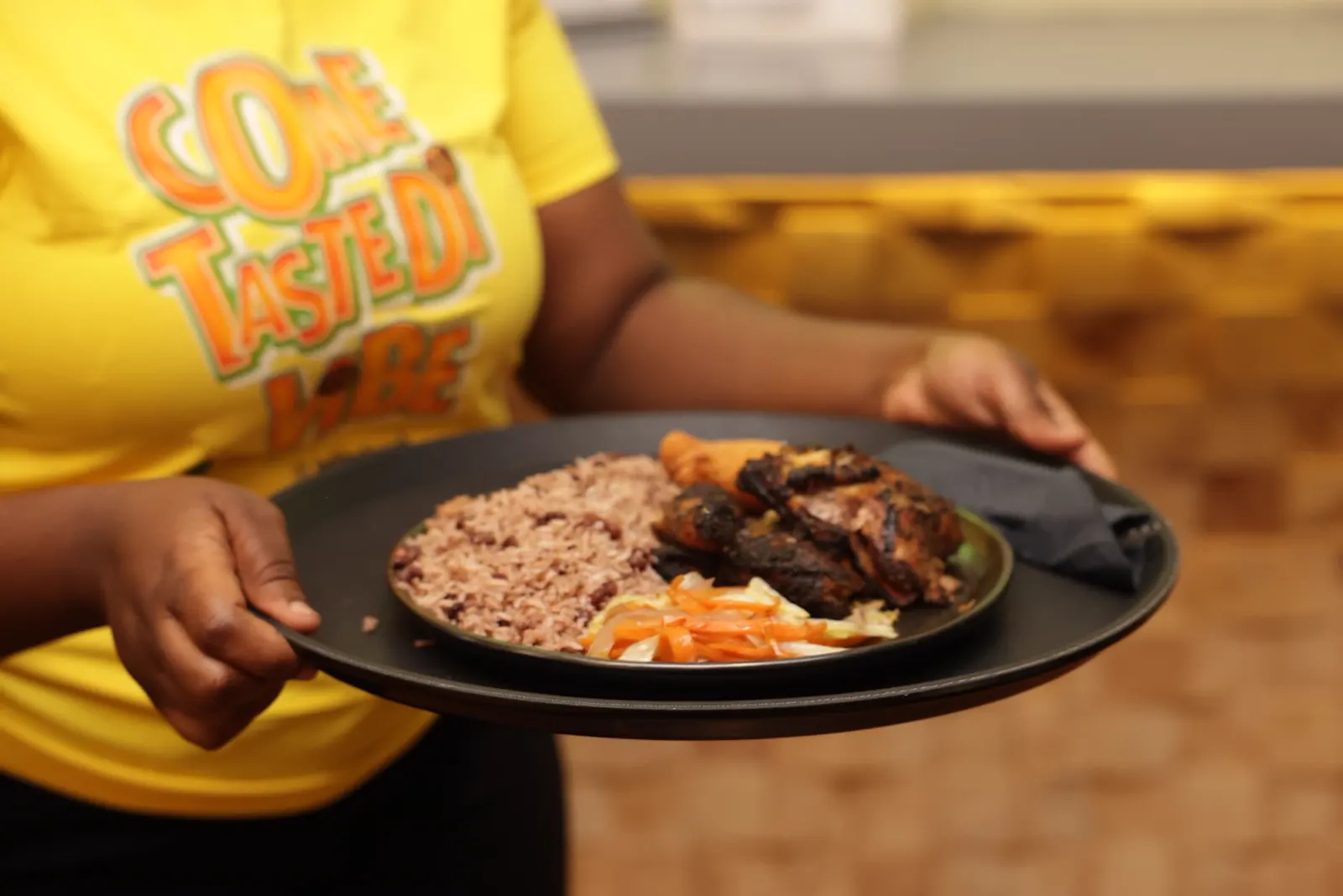 Team member serving jerk chicken with rice and peas and slaw