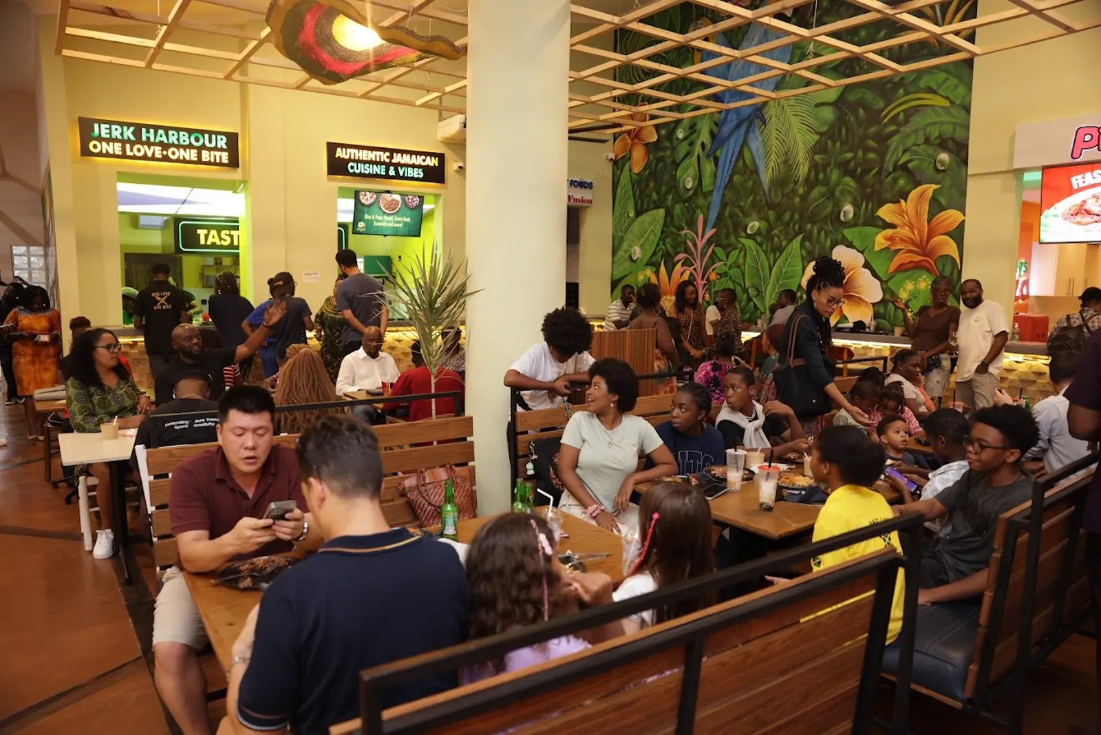 Busy Jerk Harbour dining room at Jungle Avenue Food Court with tropical mural