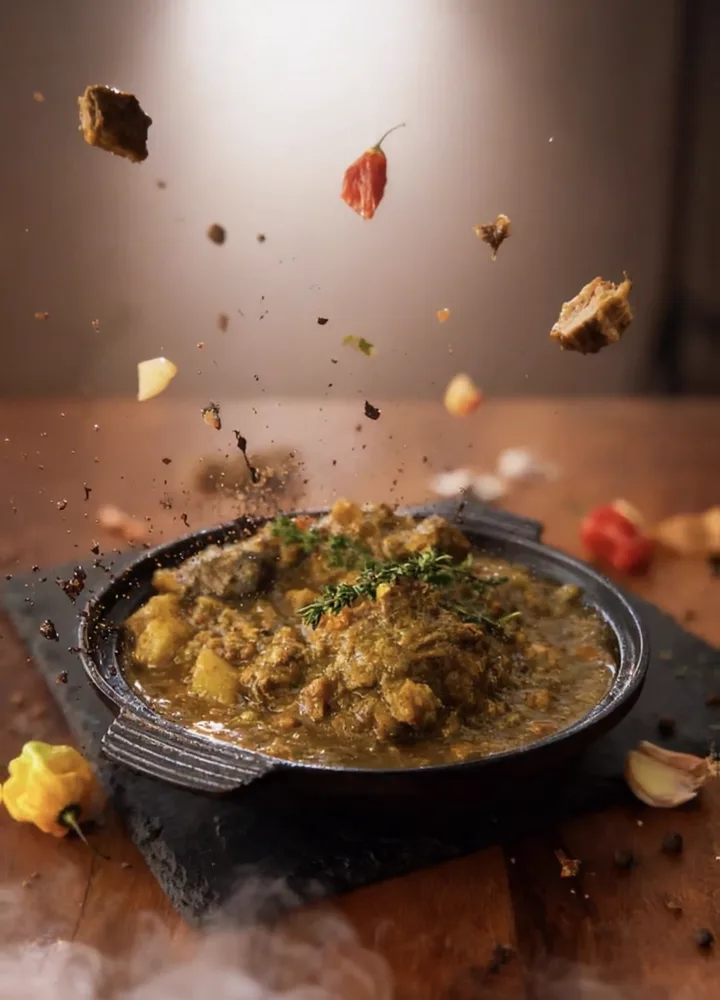 Curry goat simmering in a cast-iron dish, topped with fresh thyme