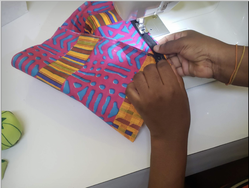 Hands guiding brightly patterned African print fabric through a sewing machine