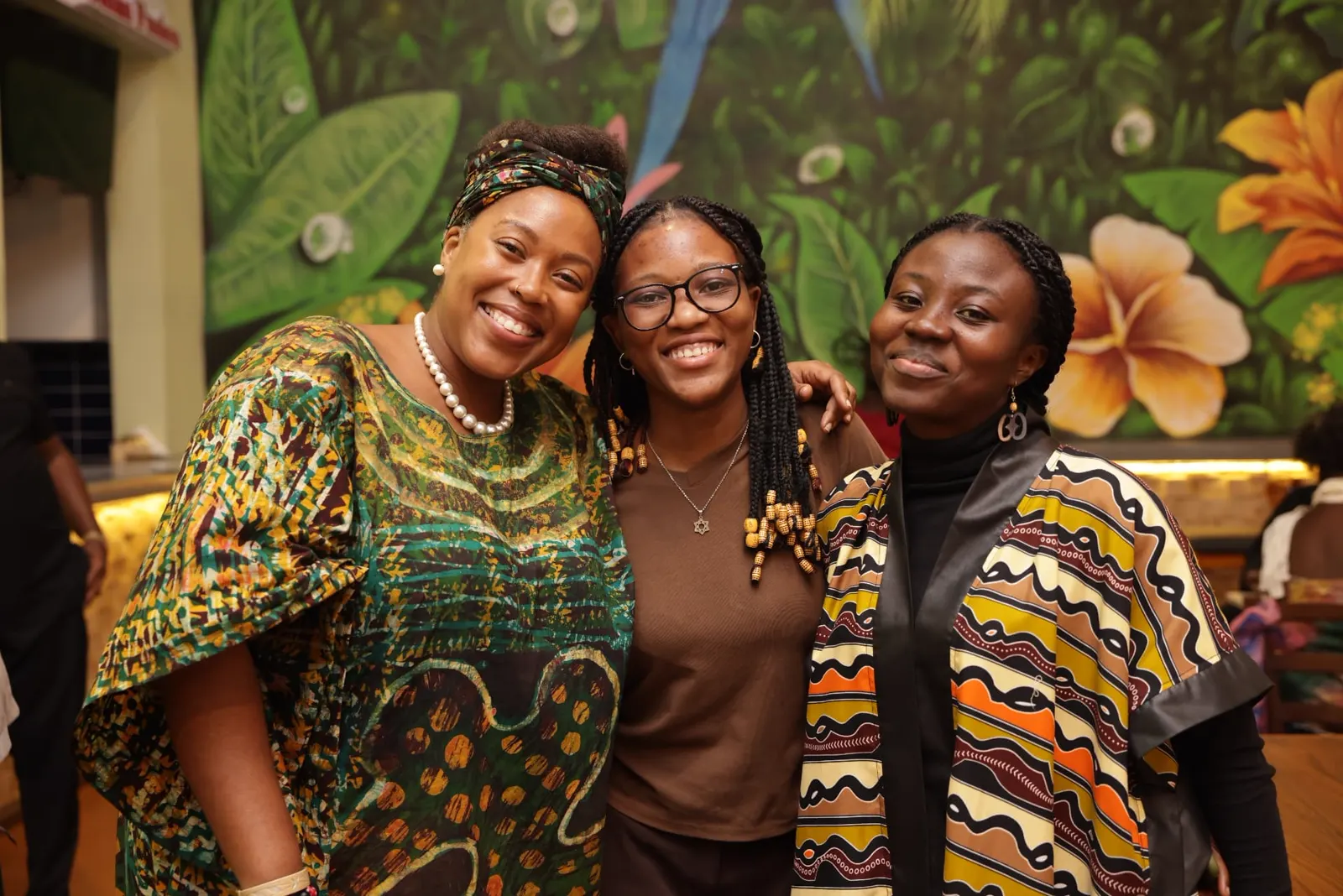 Three guests smiling in front of the tropical mural